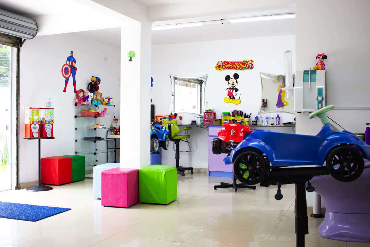 Sala de atendimento colorida com cadeiras em formato de carrinho azul e vermelho, pufes coloridos e brinquedos