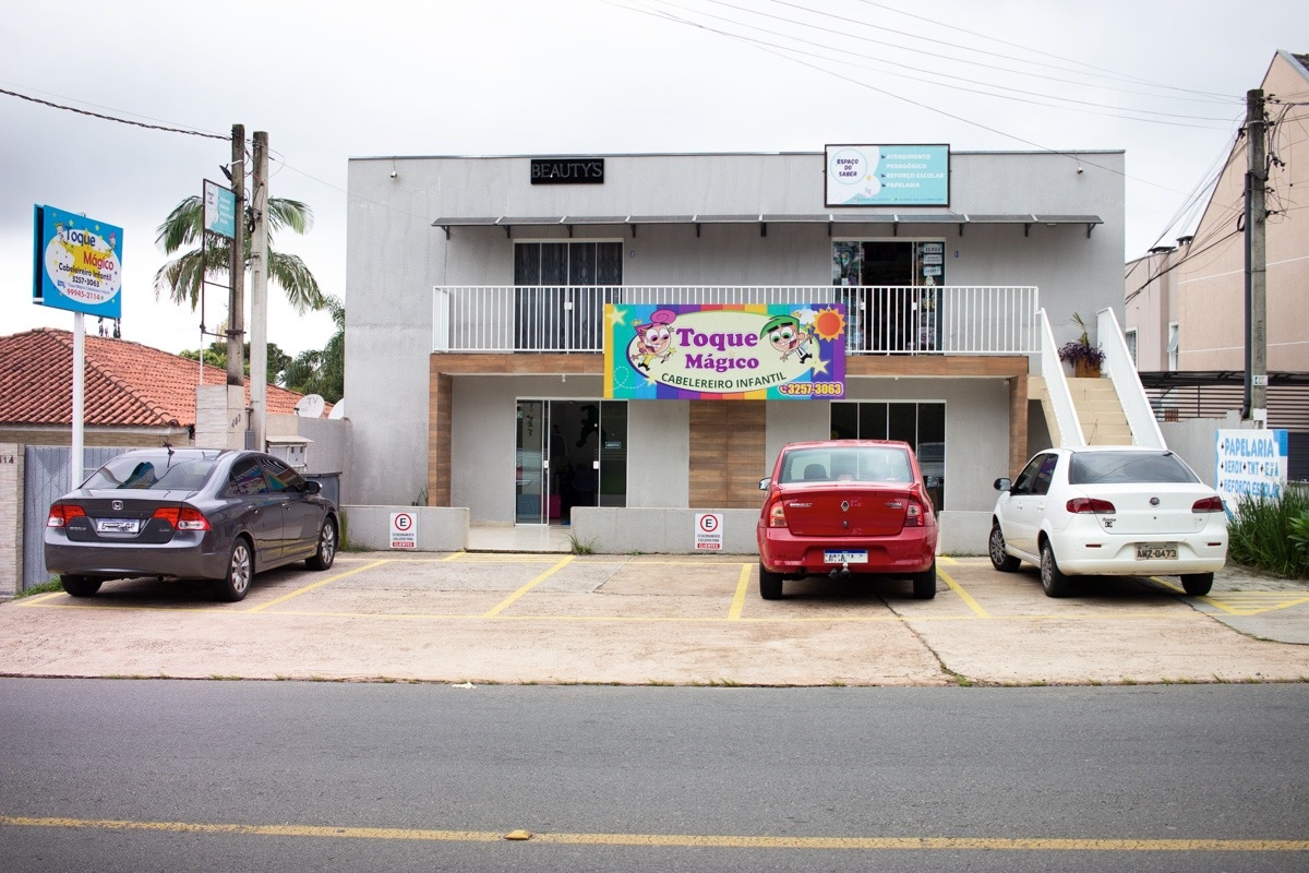 Fachada do Toque Mágico vista da rua, com placa na calçada e vagas de estacionamento exclusivas para clientes
