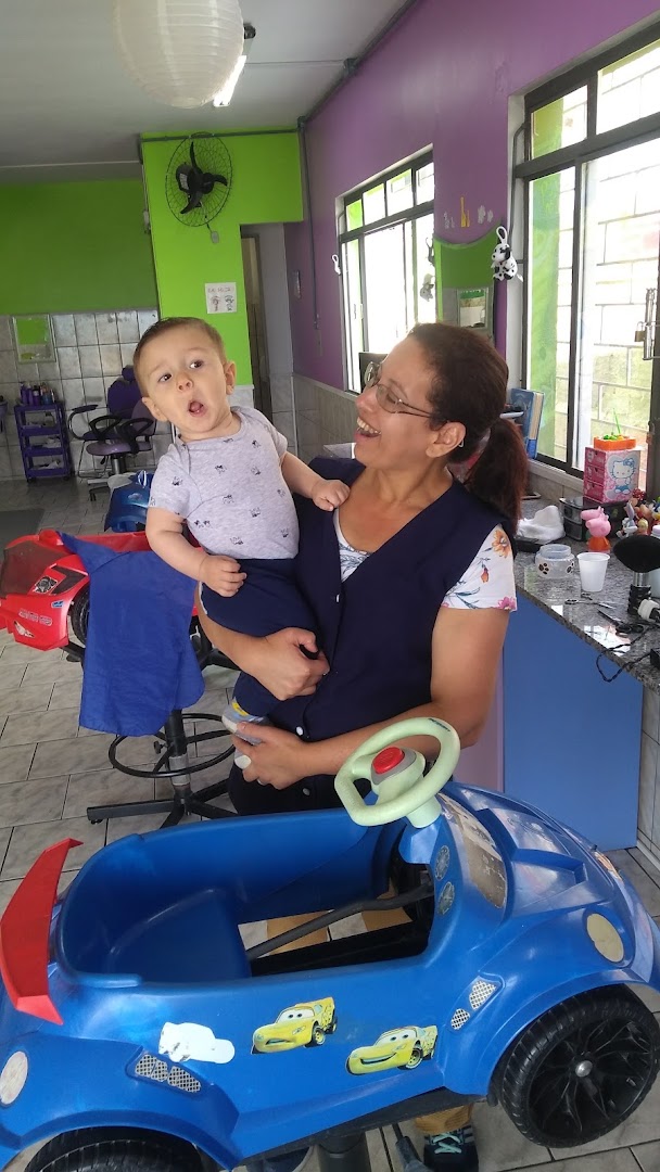 Profissional do salão sorrindo com um bebê no colo, sentado no carrinho de corte